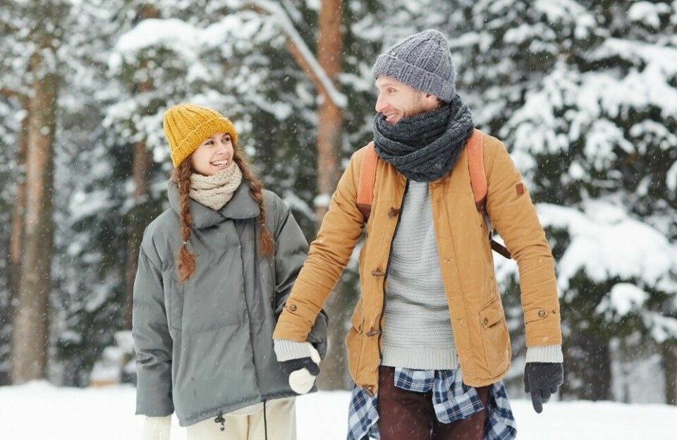 Two young backpackers in winterwear walking in the forest in snowfall in winter